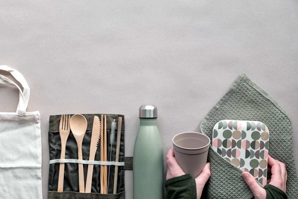 Flatlay of low impact living products - white tote bag, wood cutlery, reusable bottle