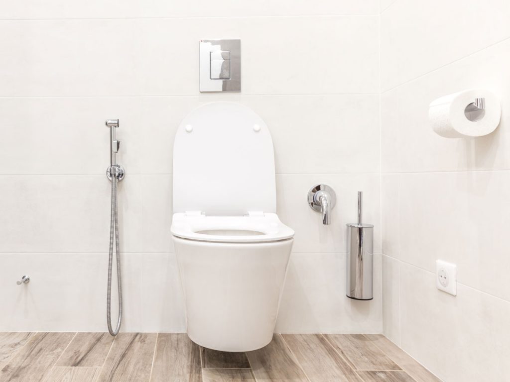 White toilet with eco friendly home improvements of external bidet and dual flush buttons.