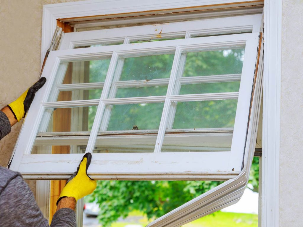 Man removing old white window from frame.