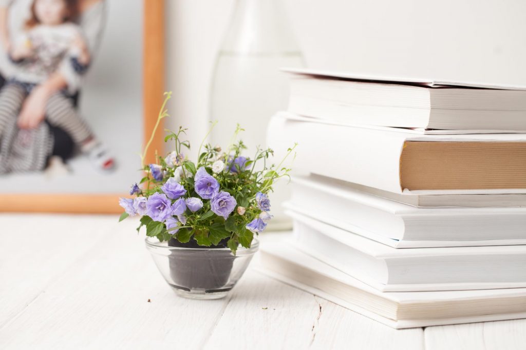 Stack of best books on simple living next to purple flowers on white table