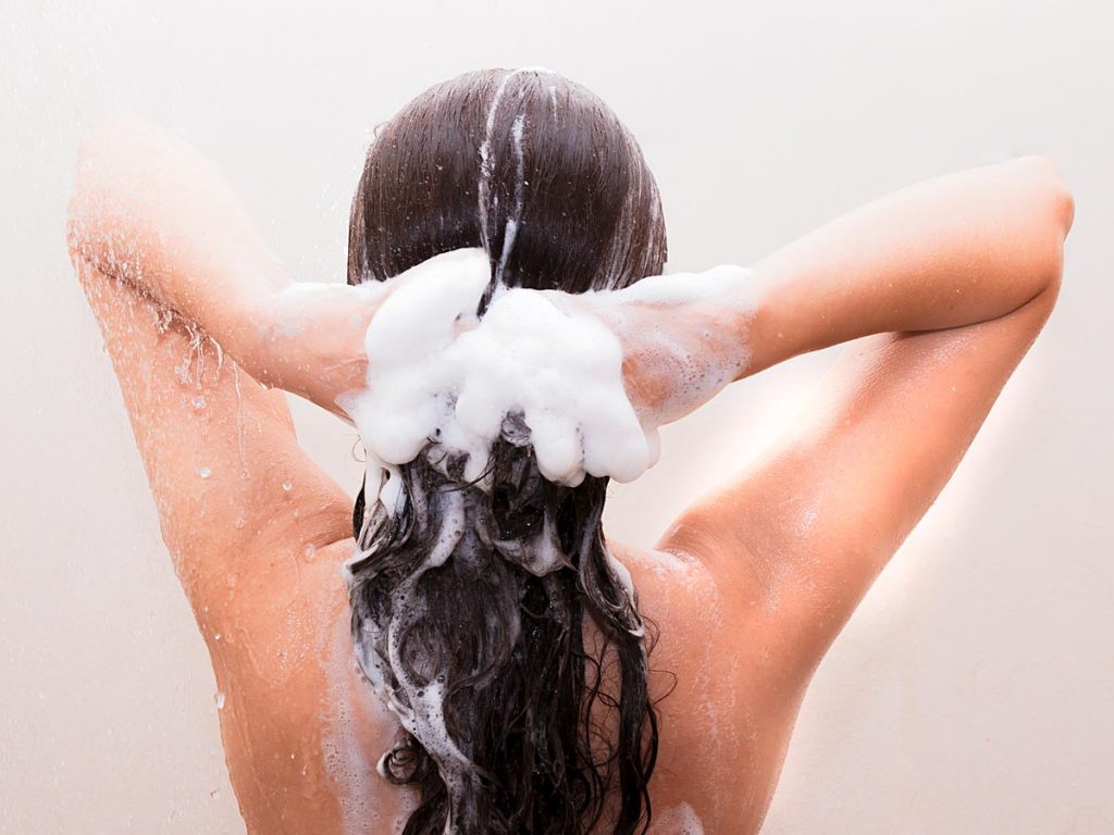 Woman washing long brown hair with zero waste shampoo bar.