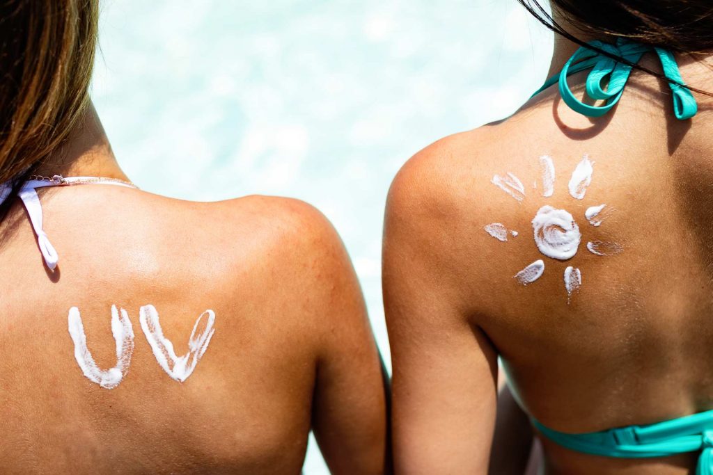 Backs of two women at pool wearing zero waste sunscreen applied with letters UV and sun pattern.