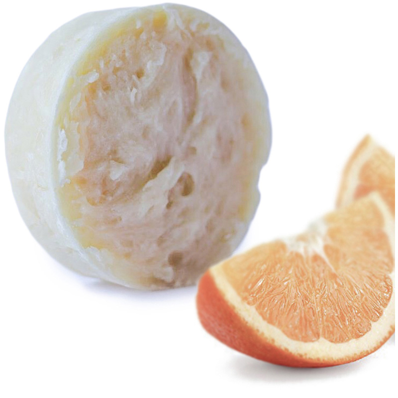 Orange slice in front of round orange shampoo bar.