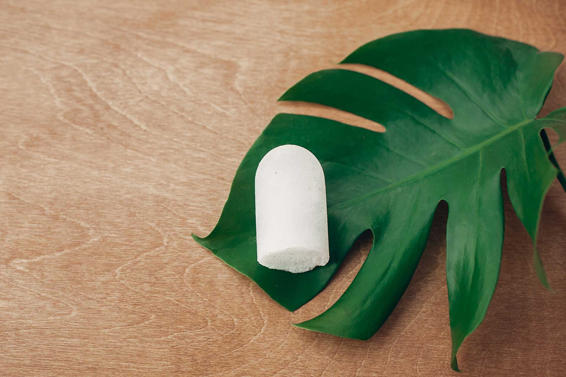 White plastic free deodorant bar on top of large green leaf.