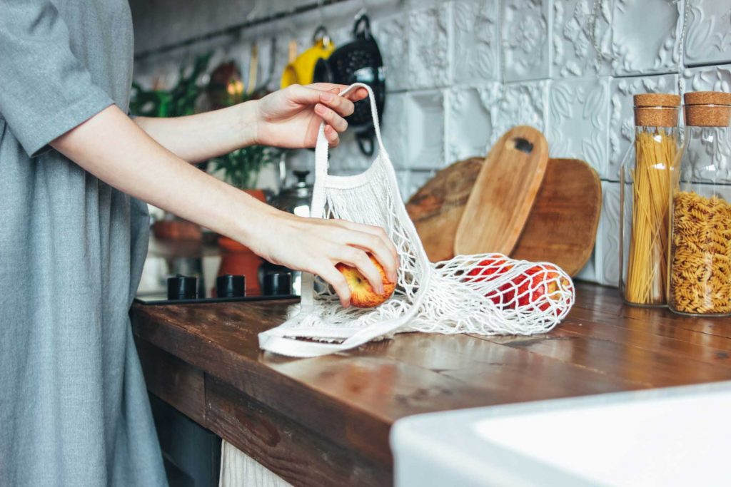 Woman in zero waste kitchen putting apples into mesh bag.