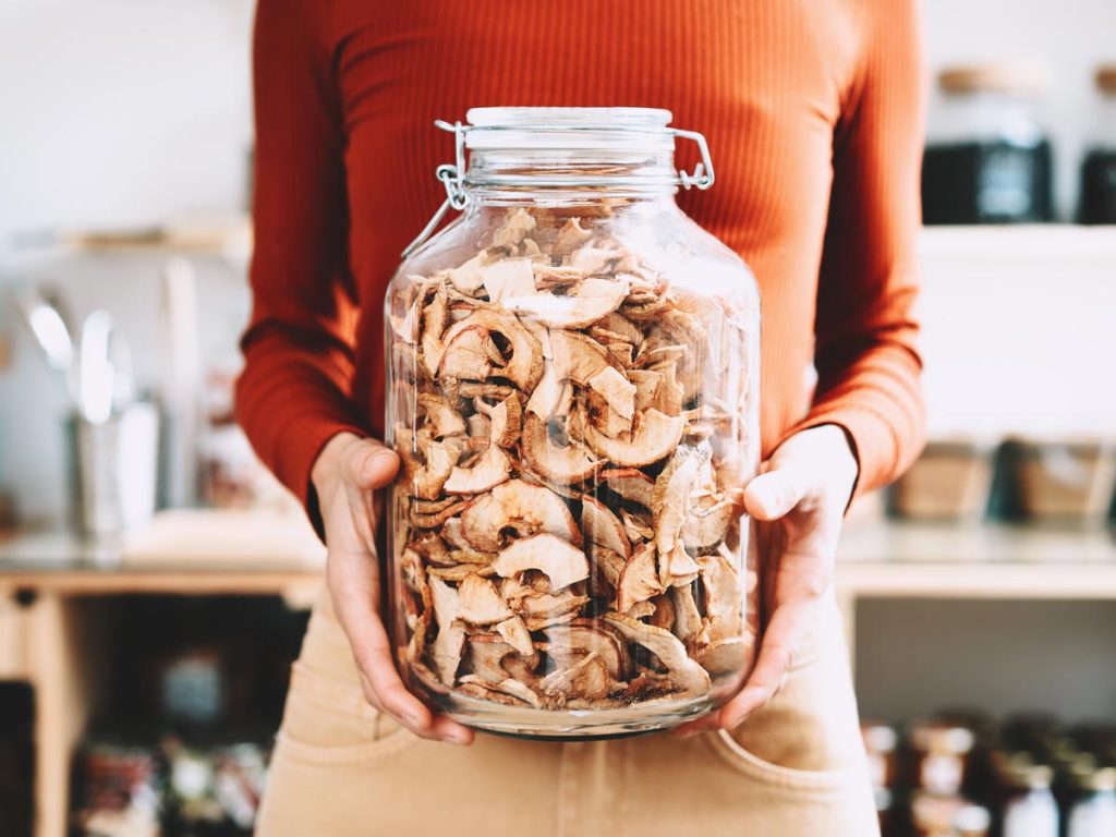 Woman in red sweater holding glass jar of dried mushroom slices.