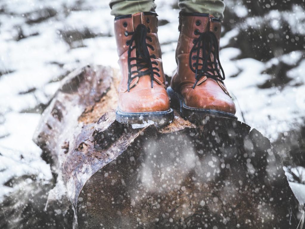 Pair of sustainable winter boots on top of log during snowstorm.