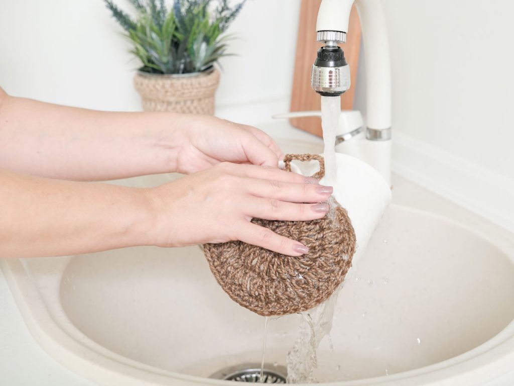 Woman washing white mug with jute dish sponge alternative over white sink basin.