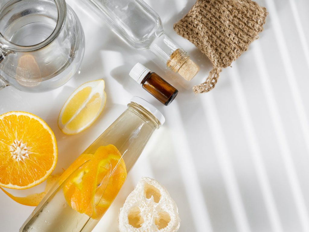 Glass jar of DIY natural fabric softener, cut orange and lemon, and natural sponge on white background.
