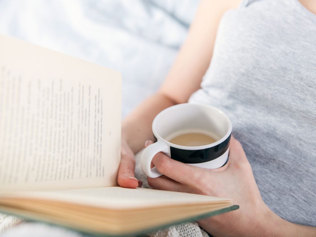 Woman reading book about living intentionally and holding coffee mug.