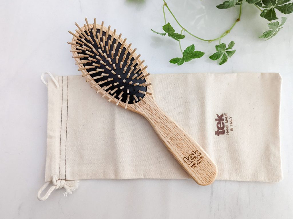 Close up of wooden zero waste hair brush on canvas bag next to green vine.