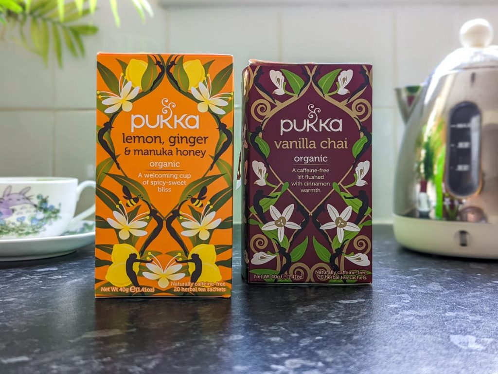 Two boxes of Pukka zero waste tea on black counter in front of kettle and tea cup.