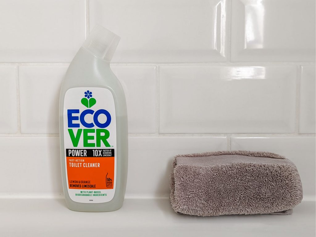 Bottle of Ecover eco friendly toilet bowl cleaner next to grey rag against white tile.
