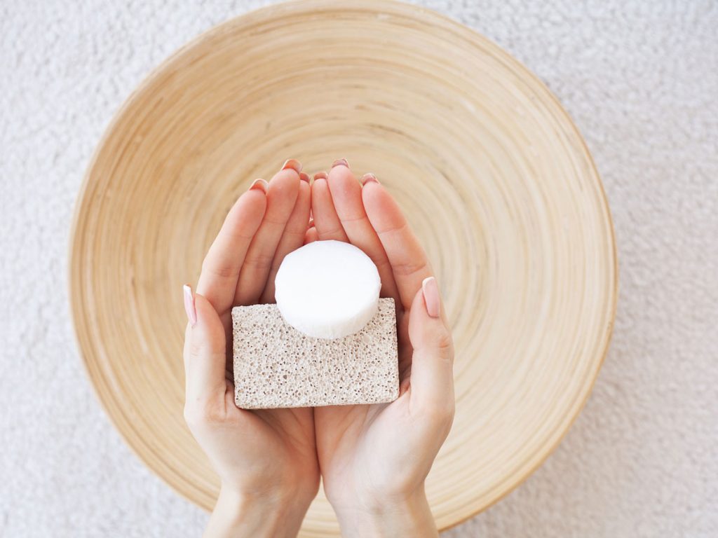 Two hands holding eco friendly toilet bowl cleaner over wooden bowl.