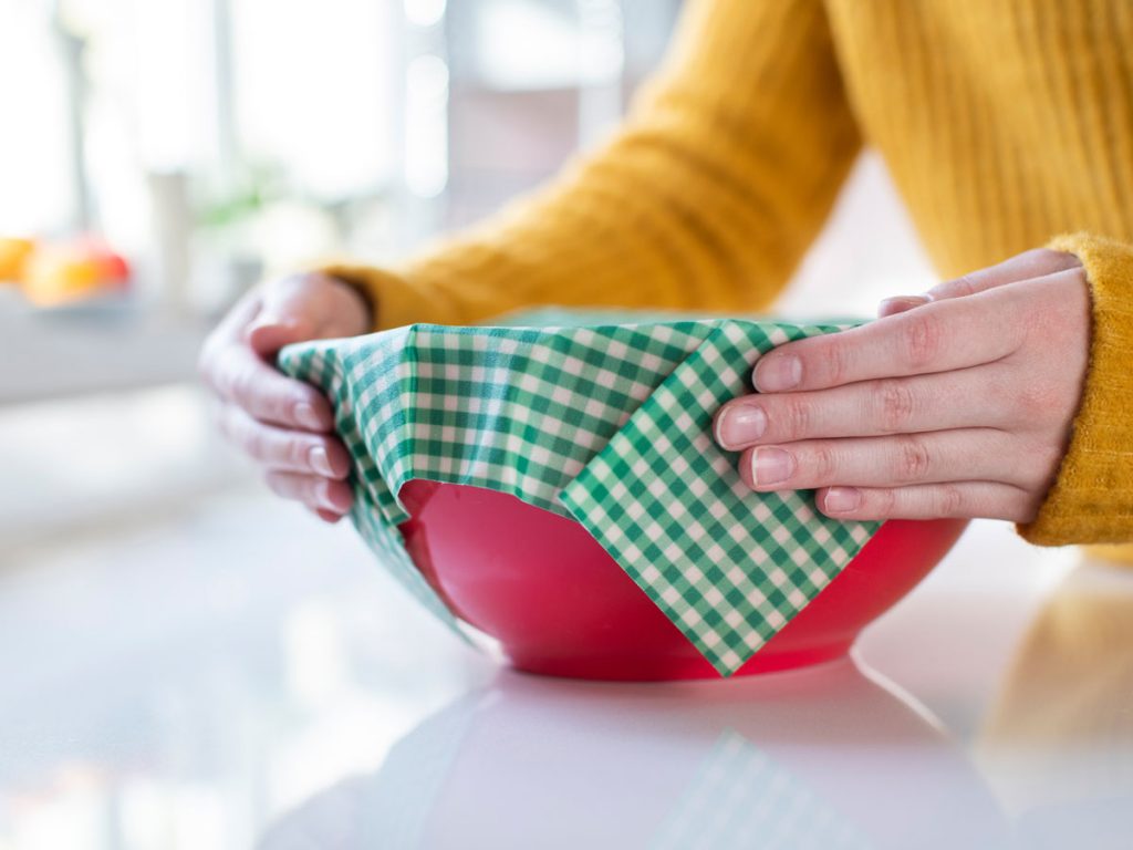 Woman putting checkered beeswax wrap on top of red bowl.