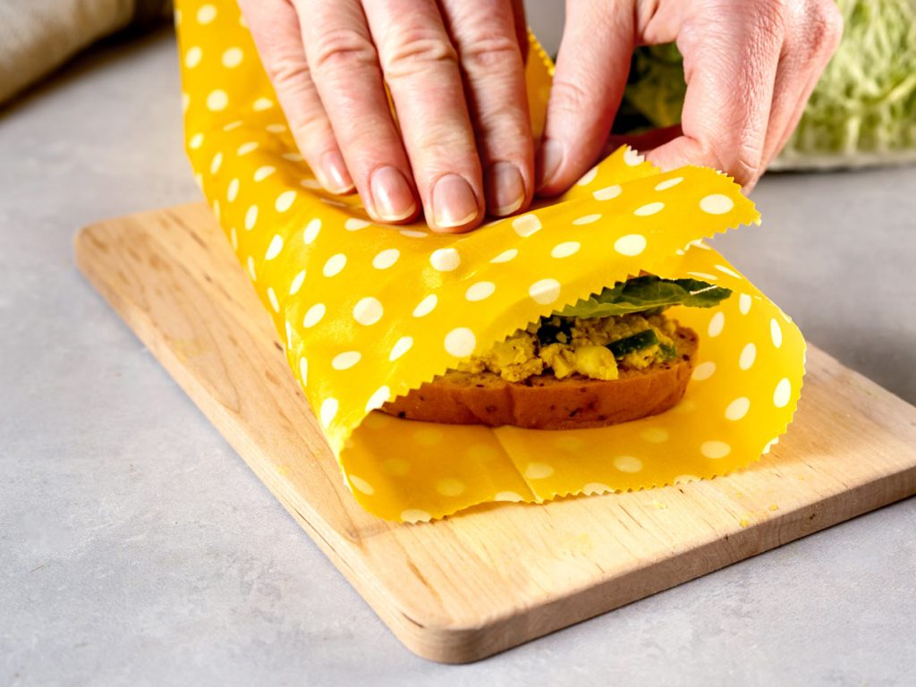 Woman wrapping sandwich in yellow polka dot reusable food wrap.